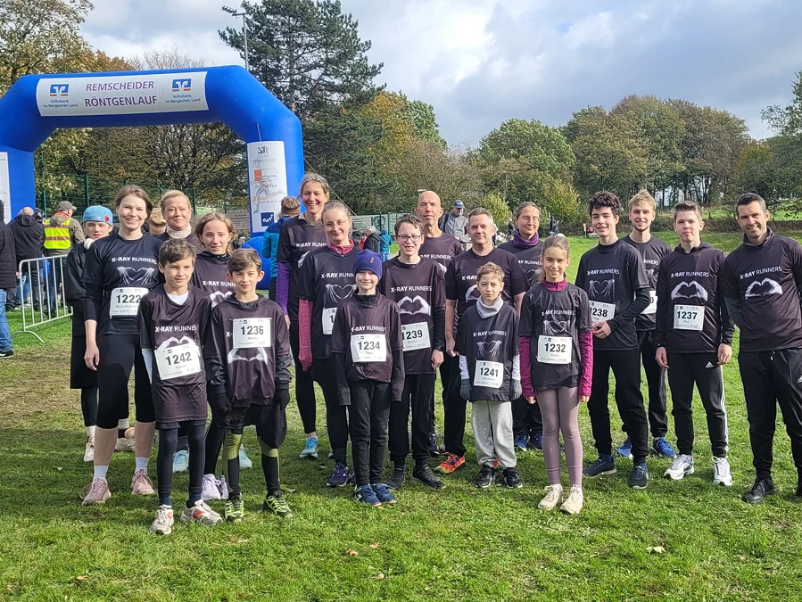 Eine Gruppe von Läufer:innen in Sportkleidung steht auf einer Wiese vor einem blauen Startbogen.